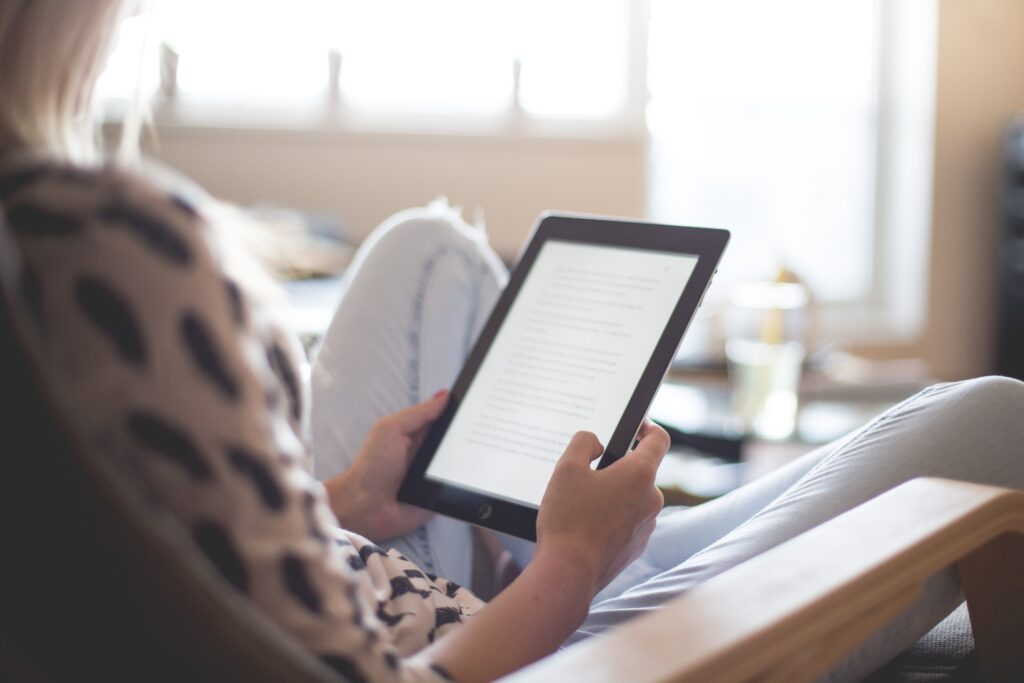 Image shows a woman reading an article on a tablet computer.